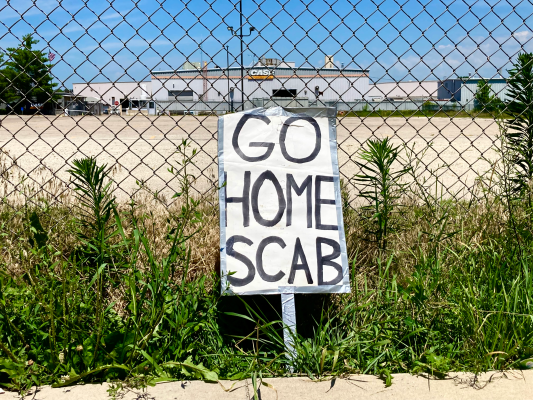 A handmade "Go Home Scab" sign leans against the fence outside the Case New Holland Plant in Burlington, Iowa, where workers have been on strike since May 2