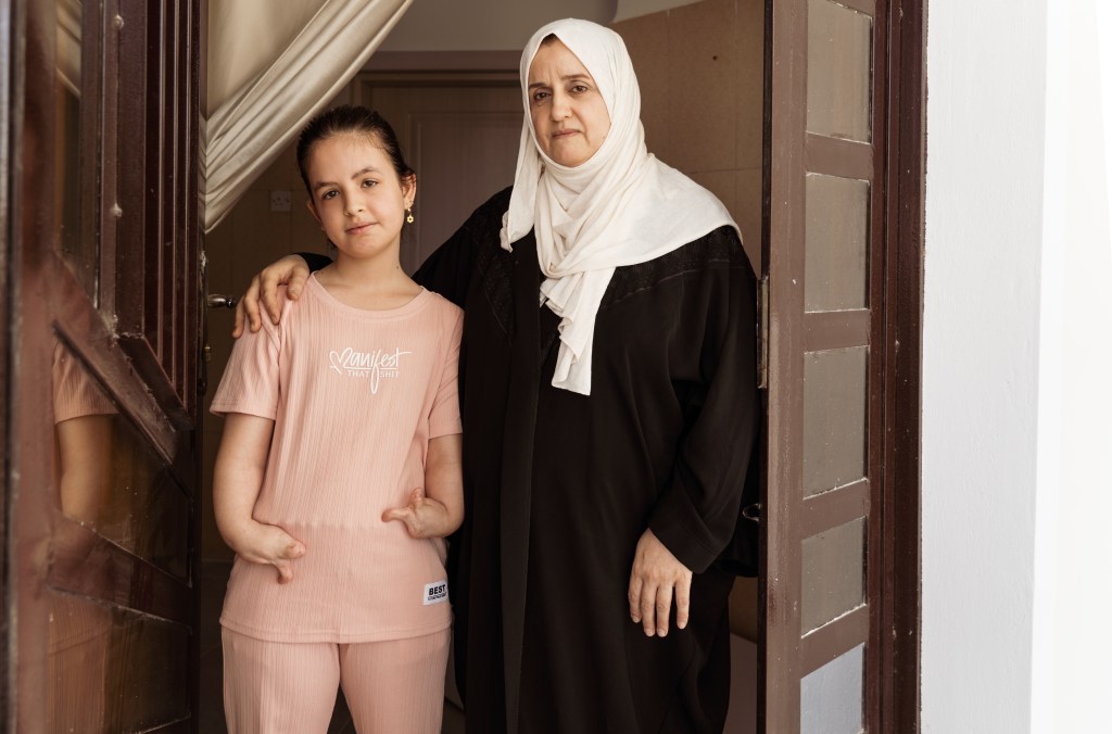 Supported by her mother outside their Fallujah home, Fatema embodies how the war never truly ended—her condition still imposing heavy medical and financial burdens on her family two decades later. Photo by Jaclynn Ashly.